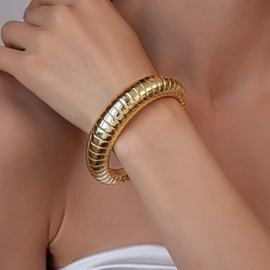 Close-up of a gold-toned chunky Tubogas style textured cuff bracelet on a model's wrist