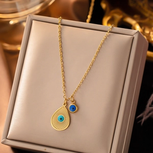 Detailed view of a gold-toned teardrop evil eye necklace on a champagne jewelry box