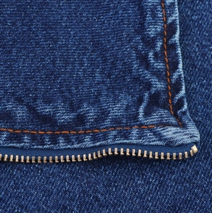 Dettaglio ravvicinato del tessuto denim blu scuro con cuciture arancioni e zip metallica