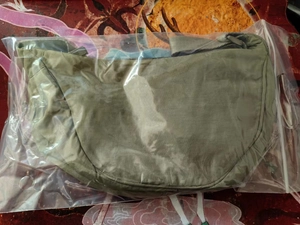 Detailed view of a green nylon dumpling crossbody bag packaged in a clear protective bag