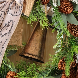 Close-up of a bronze metal bell with pine cones and a Merry Christmas ribbon on wood