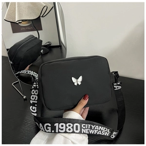 Detail of black nylon crossbody bag featuring a white butterfly buckle and wide logo strap