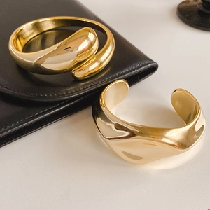 Detailed view of polished gold wavy and spiral open bangles on a minimalist white surface