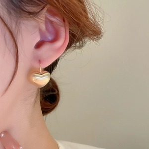 Close-up of a model wearing a brushed gold heart-shaped earring in a vintage style