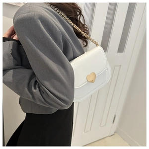 Detail of white patent leather crossbody bag with a large gold heart-shaped metal buckle
