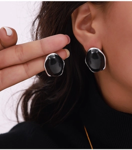Close-up of model wearing black irregular enamel earrings with gold metal frame accents