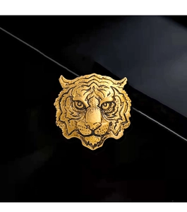 Detailed view of a golden metal tiger head brooch on a black reflective surface