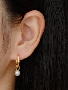Close-up of a vintage S925 silver hoop earring with a white pearl drop on a model's ear