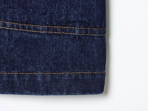Gros plan sur le tissu denim indigo foncé avec des coutures contrastées orange détaillées