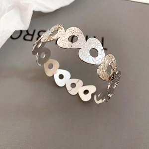 Detail of silver hollow heart bracelet featuring fine floral and leaf engravings on metal
