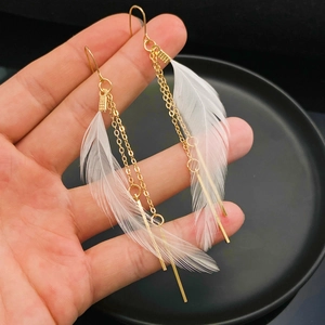 Primer plano de pendientes largos con plumas blancas y flecos metálicos dorados finos