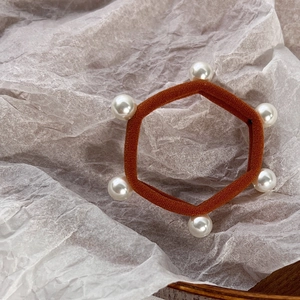Detailed view of elastic hair tie with white pearls on brown fabric over paper texture