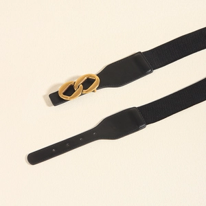 Detail of black elastic belt with gold double ring buckle and leather ends on beige background