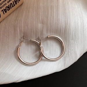 Detailed shot of silver hoop earrings with glossy finish on a white textured background