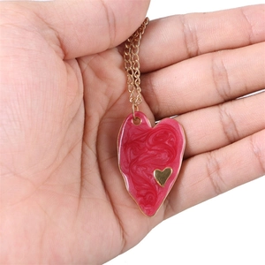 Detail view showing a red enamel heart pendant necklace held in hand for scale