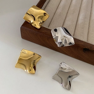 Minimalist gold and silver wavy earrings on a wooden jewelry tray in high-polish finish
