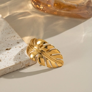 Golden stainless steel monstera leaf ring on a textured stone with elegant lighting