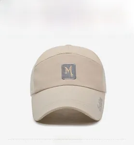 Detail of beige mesh baseball cap featuring an M patch and embroidered brim for sun protection