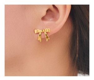 Close-up detail of a minimalist golden bow-shaped stud earring worn on the earlobe