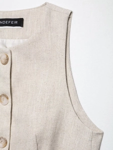Detail of oatmeal linen vest featuring textured fabric and decorative round buttons