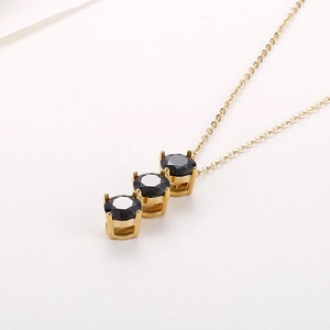 Dettaglio di una collana d'oro con tre pietre preziose nere verticali su uno sfondo bianco