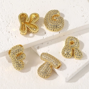 Gold plated bubble letter necklaces with cubic zirconia stones on white stone surface