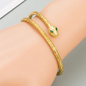 Macro shot of gold snake bracelet showing detailed scales and green gemstone eyes