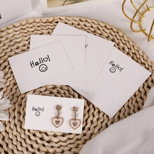 Gold heart pendant earrings with crown detail and pearls on a smiling face display card