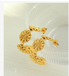 Detailed view of 18k gold daisy flower C-shaped hoop earrings on glass bowl