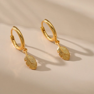Detailed view of gold leaf charm hoop earrings with fine texture on warm background