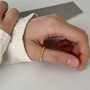 Detail of stacked gold heart ring on thumb with elegant white pleated sleeve cuff