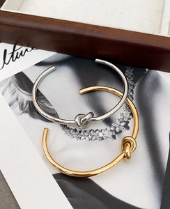 Detail of minimalist knot open bracelets in gold and silver finish on artistic background