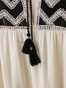 Close-up of bohemian dress featuring intricate crochet patterns and black gold tassels