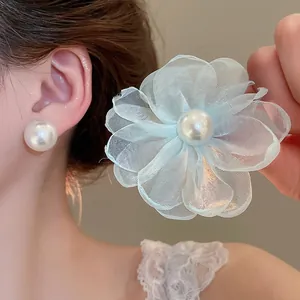 Elegant asymmetrical pearl stud earrings with light blue chiffon flower on a female model