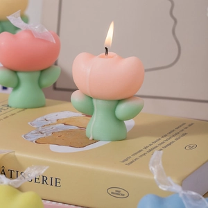 Scented tulip candle in pink and green, lit and placed on a decorative book base