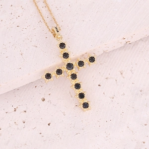 Detailed macro view of 18K gold cross pendant with black zircon stones on stone background