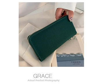 Detail of forest green canvas long wallet with golden zipper held by hand on stylish background
