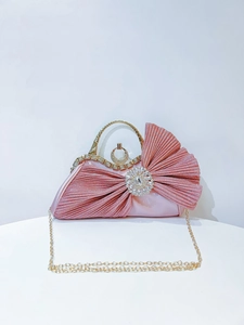 Detailed view of pink satin evening bag with crystal bow, gold handle and chain strap