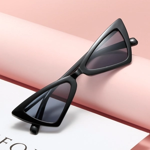 Fashionable black triangular cat eye sunglasses with dark lenses on a pink pedestal