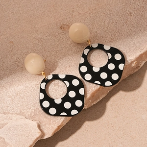 Detail of vintage acrylic black and white polka dot square earrings on stone texture
