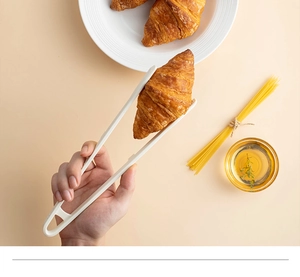 Close-up of white heat-resistant silicone food tongs picking up a fresh croissant