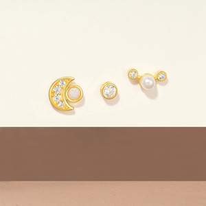 Detail of 925 silver earring set featuring gold moon, single diamond, and pearl stud designs