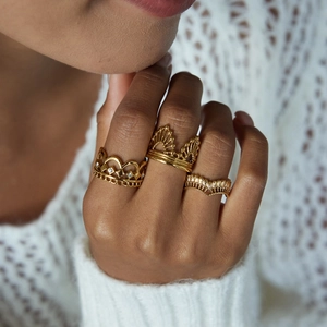 Detail of three stacked gold-plated crown rings with cubic zirconia on model's finger