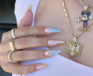 Détail d'ongles stiletto Y2K avec effet aurore, bordure dorée et bijoux de mode