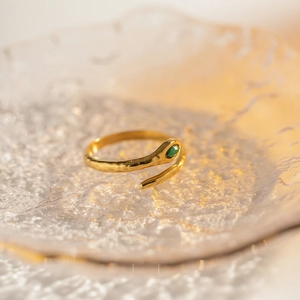 Details eines schlangenförmigen Goldrings mit grünem Edelstein auf Glasoberfläche