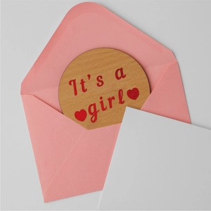 Wooden round 'It's a girl' card with pink envelope and white note for baby reveal party