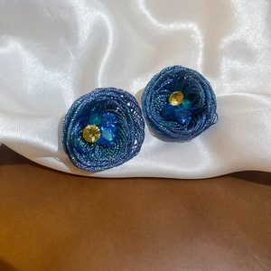 Close-up of dark blue woven earrings with multi-color crystals on white silk