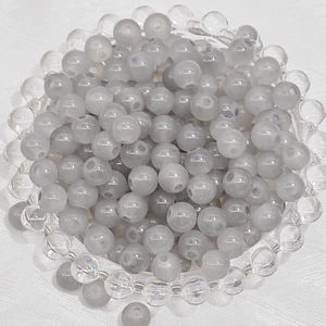 Top view of translucent grey round glass beads with holes in a clear tray for DIY jewelry
