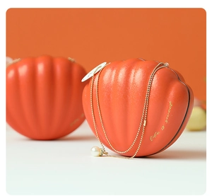 Macro detail of orange shell-shaped gift box with gold text and a pearl pendant