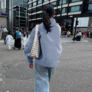 Rear view of a light blue polo collar jacket with a white studded crossbody bag in the city